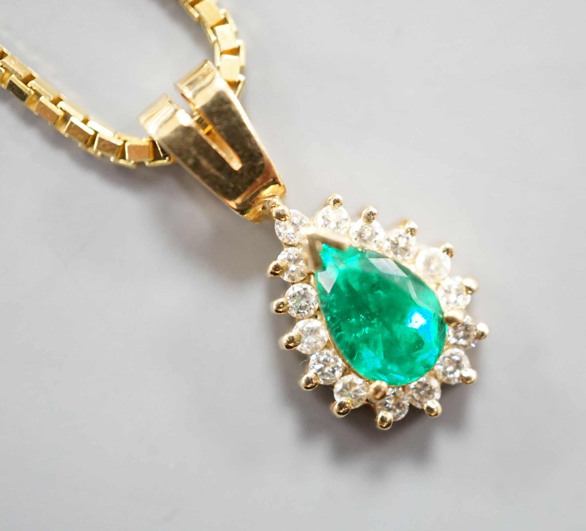 A modern 18k, emerald and diamond cluster set pear shaped pendant, overall 21mm, on an 18k chain, 43cm